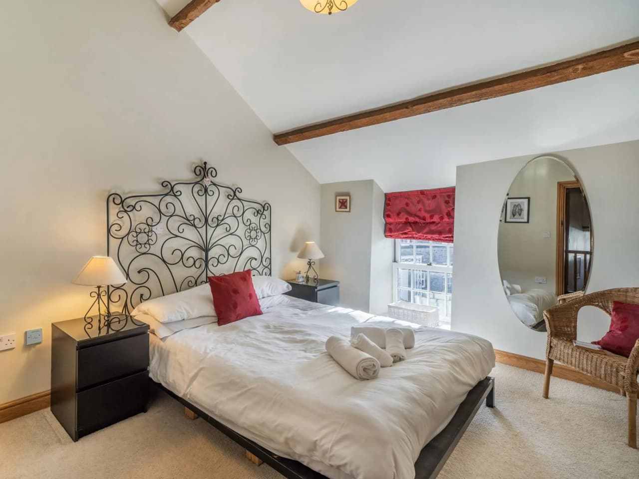 A view of the main bedroom with a large queen sized bed, side tables, mirror and a chair