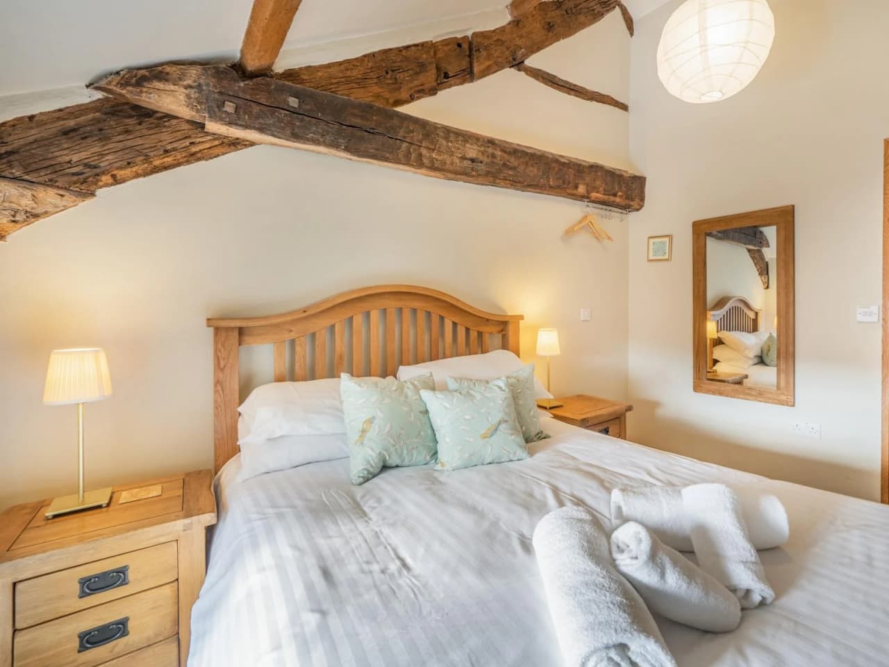 The second bedroom with a double bed, side tables, mirror and exposed old origial ceiling joists